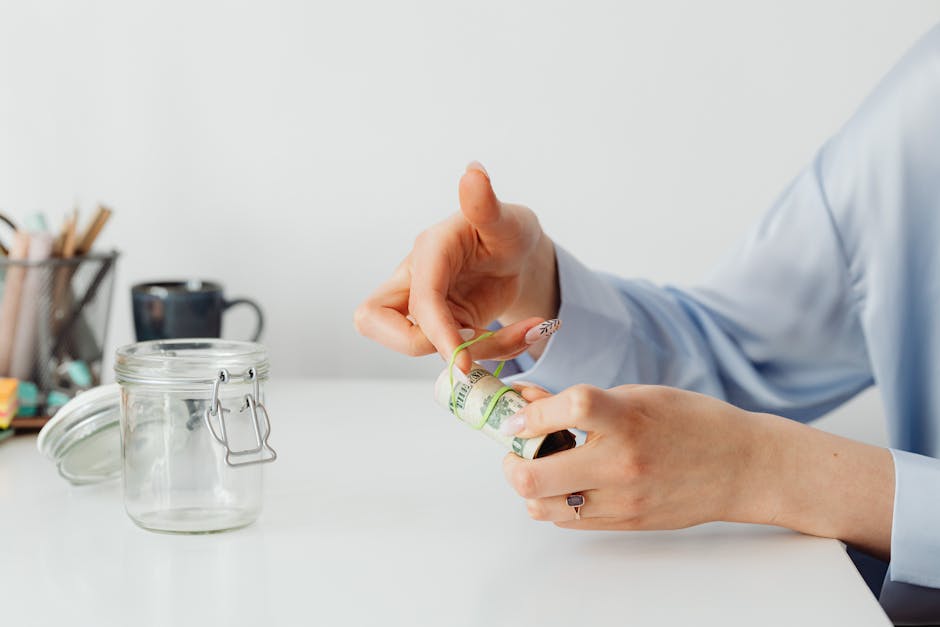 Hands bundling cash with a rubber band near a glass jar, representing the cost savings of consolidating business software